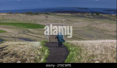 AUSTURLAND, ISLAND, 20. JUNI: Eine ältere Frau in einem grünen cape und mit Wanderstöcken wandert am 20. Juni 2013 in Austurla in der Nähe des Wasserfalls Hengifoss Stockfoto