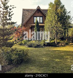 Gemütliches Landhaus aus Holz auf grüner Wiese gelegen und am sonnigen Tag von Bäumen umgeben Stockfoto