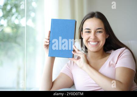 Glückliche Frau, die vor der Kamera leeres Papierbuch zu Hause zeigt Stockfoto