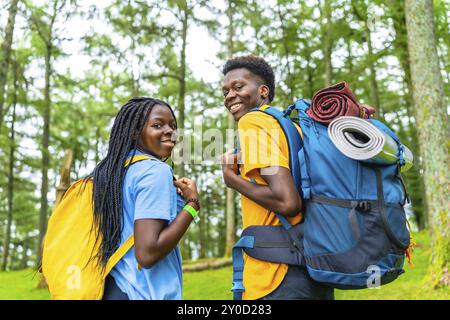 Rückansicht afrikanischer Freunde, die sich vor der Kamera lächeln, während sie durch den grünen Wald laufen Stockfoto