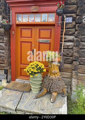 Eine orange Holztür mit dekorativen Blumentöpfen und einer Holzskulptur vor einer rustikalen Holzhütte, UNESCO-Weltkulturerbe, Fußgängerzone, Stockfoto