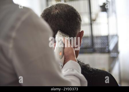 Nahaufnahme eines Friseurs, der einem Mann die Haare mit einem Rasierer zuhause schneidet Stockfoto