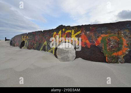 Strandszene mit einer Betonkonstruktion, die mit farbenfrohen Graffiti auf Schiffswracks bedeckt ist, teilweise in Sand unter einem bedeckten Himmel vergraben, Norderney, East Frisi Stockfoto