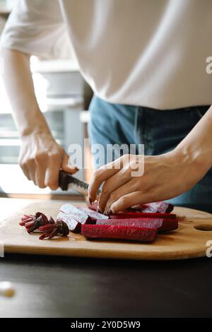 Nahaufnahme von Frauenhänden, die frische Bio-Rüben in Streifen in der Küche schneiden Stockfoto