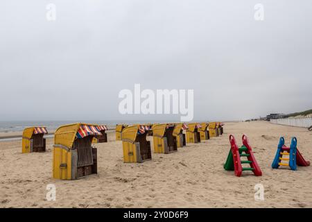 Ein ruhiger Strand verfügt über mehrere leuchtend gelbe und rote Strandhütten am Ufer, während farbenfrohe Spielplatzrutschen in Grün und Rot auf dem Sand stehen Stockfoto