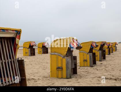 Ein ruhiger Strand verfügt über mehrere leuchtend gelbe und rote Strandhütten am Ufer, der bewölkte Himmel schafft eine ruhige Atmosphäre am Strand ohne pe Stockfoto
