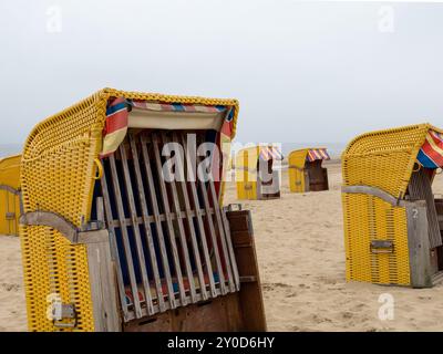Ein ruhiger Strand verfügt über mehrere leuchtend gelbe und rote Strandhütten am Ufer, der bewölkte Himmel schafft eine ruhige Atmosphäre am Strand ohne pe Stockfoto