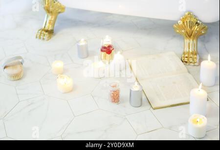 In der Nähe von Kerzen, einem Buch, einem Glas Champagner in der Badewanne auf der gefliesten Marmorboden Stockfoto