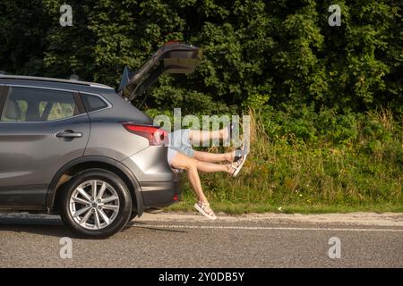 Humorvolle Szene der Beine, die vom SUV Trunk Road Trip hervorragen Stockfoto