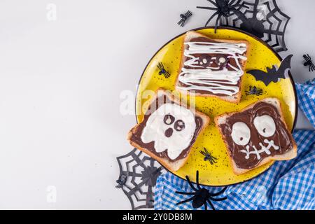 Lustige Halloween-Charaktere toasten Sandwiches mit Nüssen, Schokoladenbutter, Paste, Banane und geschmolzenem Marshmallow oder Joghurtnarben Dekor. Kreatives Halloween Stockfoto