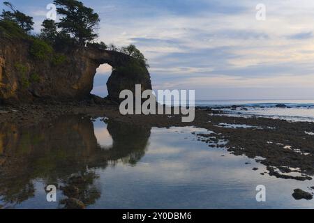 Ein bewölkter Abendhimmel nach Sonnenuntergang und eine große natürliche BrückenFelsformation spiegeln sich in einem ruhigen Pool aus Ozeanwasser bei Ebbe auf Neil Island wider Stockfoto