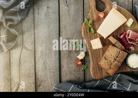 Italienische Küche Konzept flach Lay. Schneidebrett, Parmesan-Käsestückchen, geriebener Käse in schwarzer Schüssel, dünn geschnittener Schinken, Kirschtomate, Basilikumblätter b Stockfoto