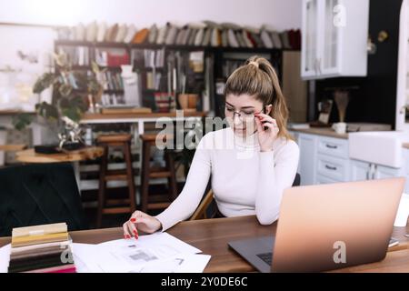 Eine Innenarchitektin arbeitet an einem neuen Projekt, Frau hält Papierplan mit Stift. In Anbetracht der Entscheidung. Laptop auf dem Schreibtisch. Denken Sie über Neues nach Stockfoto