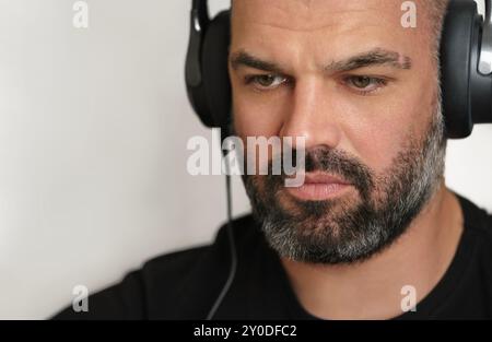 Hübscher bärtiger Mann mittleren Alters mit Kopfhörern, die sich auf die Arbeit konzentrieren. Kopfschuss Stockfoto