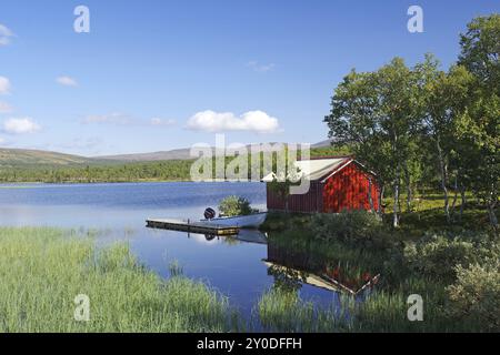 Rote Hütte an einem ruhigen Seeufer, umgeben von Bäumen unter blauem Himmel, Idyll, Glomma, Roeros, Troendelag, Norwegen, Europa Stockfoto