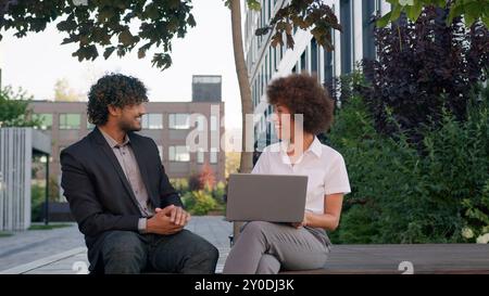 Multirassische Geschäftskollegen Kollegen Partner Freunde afrikanische Geschäftsfrau arabischer indischer Geschäftsmann auf der Bank in der Stadt mit Laptop Erfolg Stockfoto