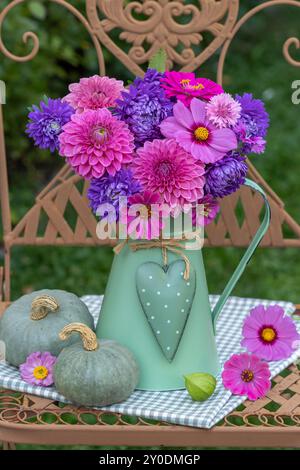 Blumenstrauß aus violetten Sommerastern, rosa Dahlien und Zinnien in einer alten Kanne auf einem Gartenstuhl Stockfoto