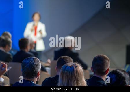 Geschäftsleute hören während der Konferenz aufmerksam dem Sprecher zu. Konzentrieren Sie sich auf das Publikum, während der Sprecher auf der Bühne vor verschwommenem Hintergrund präsentiert. Stockfoto