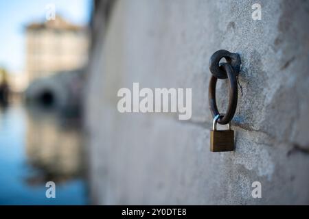 Ein kleines Schloss an einem alten Metall-Festmacherring. Steinmauer an einem Flussufer in Europa, geringe Tiefe des Feldes, Flusswasser und Gebäude im Hintergrund, nein Stockfoto