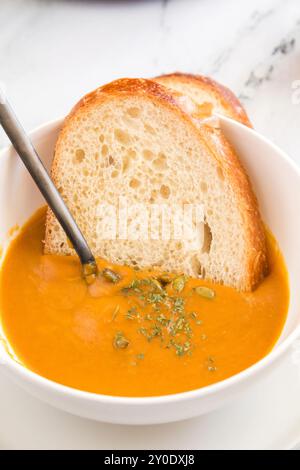 Brotscheibe in Butternusskürbis-Suppe mit Kräutern getaucht Stockfoto