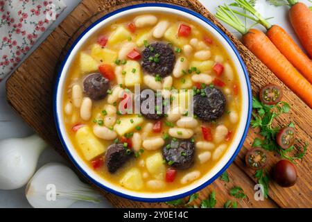 Bohneneintopf mit Schwarzpudding, Paprika und Kartoffeln. Tisch mit Draufsicht und Dekoration. Stockfoto