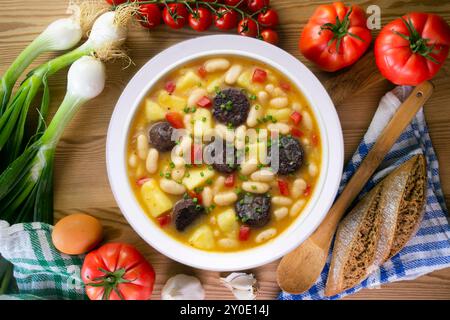 Bohneneintopf mit Schwarzpudding, Paprika und Kartoffeln. Tisch mit Draufsicht und Dekoration. Stockfoto