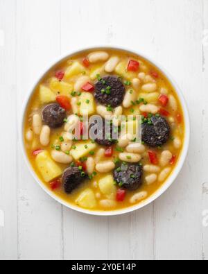 Bohneneintopf mit Schwarzpudding, Paprika und Kartoffeln. Tisch mit Draufsicht und Dekoration. Stockfoto