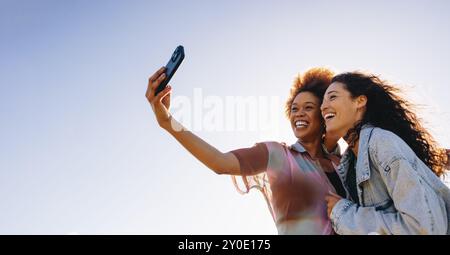 Glückliche Freundinnen in ihren 20ern, die zusammen ein Selfie machen. Positive Emotionen und Freundschaften im Freien an einem hellen, sonnigen Tag festhalten. Stockfoto
