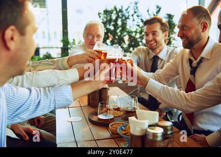 Eine Gruppe fröhlicher Männer, Geschäftsleute treffen sich in einem Café im Freien, zwitschern Gläser mit Lagerbier und feiern einen erfolgreichen Deal. Stockfoto