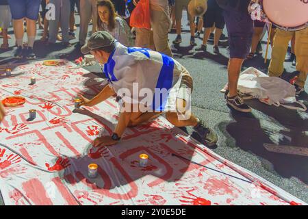 Haifa, Israel - 01. September 2024: Symbolische Präsentation blutiger Hände mit Gedenkkerzen und protestierender Menschenmenge, Teil einer abendlichen Kundgebung, Stockfoto