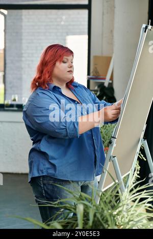 Eine Frau in Übergröße in blauem Hemd und Jeans konzentriert sich auf eine leere Leinwand. Stockfoto