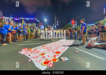 Haifa, Israel - 01. September 2024: Symbolische Darstellung blutiger Hände und protestierender Menschenmenge, Teil einer abendlichen Kundgebung, die eine Geisel fordert Stockfoto