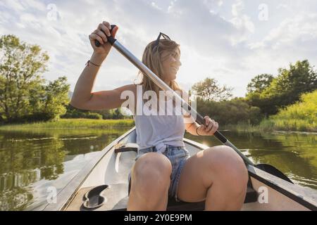 Lächelnde Frau, die ein Kanu paddelt, entspannt und genießt die natürliche Umgebung und den sonnigen Tag, Vorderansicht. Kanu- und Freizeitkonzept. Stockfoto