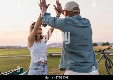 Glückliches junges Paar bei einer Kanufahrt, die High 5 auf einem wunderschönen grünen See gibt Stockfoto