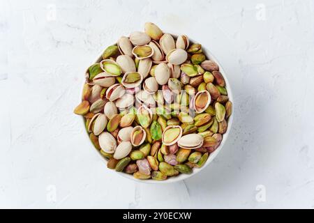 Blick von oben auf eine weiße Schüssel gefüllt mit grünen und violetten Pistazien, schalen und ungeschalen Pistazien Stockfoto