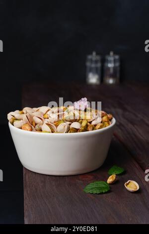 Mit und ohne Schale gefüllte weiße Schüssel mit Pistazien auf einem dunklen hölzernen rustikalen Tisch Stockfoto