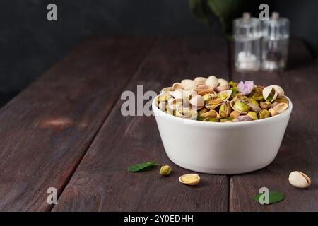 Weiße Schüssel mit Pistazien auf einem dunklen Holztisch mit verstreuten Nüssen, Bartisch, Biersnack Stockfoto