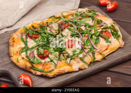 Eine köstliche neapolitanische Pizza mit Sardellen, Kapern, Kirschtomaten, frischem Gemüse und roten Zwiebeln, serviert auf einem Holzbrett Stockfoto