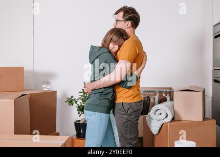 Mann warm umarmt Frau mit Liebe in einem neuen Zuhause, bewegt ungepackte Kartons, nimmt sich einen Moment, um Umzug und Umzug zu feiern Stockfoto