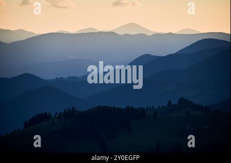 Die sanften Blautöne der mehrschichtigen Bergketten erstrecken sich bis in die Ferne unter dem Abendhimmel und schaffen eine ruhige und stimmungsvolle Landschaft mit sanften Steigungen und einem Gefühl von Weite. Stockfoto