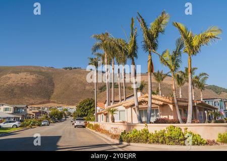 Pismo Beach, Kalifornien, USA. Juli 2024. Moderne und traditionelle Häuser mit Palmen säumen eine sonnige Straße vor dem Hintergrund sanfter Hügel. Stockfoto