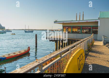 Morro Bay, Kalifornien, USA. Juli 2024. Das Restaurant blickt auf die Bucht mit Blick auf den Morro Rock und die Boote im Wasser. Stockfoto