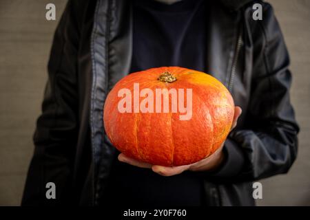 Ein kleiner orangener Kürbis in den Händen eines Mannes auf einem dunklen, verschwommenen Hintergrund. Konzept für Halloween, Thanksgiving und Erntetag. Stockfoto