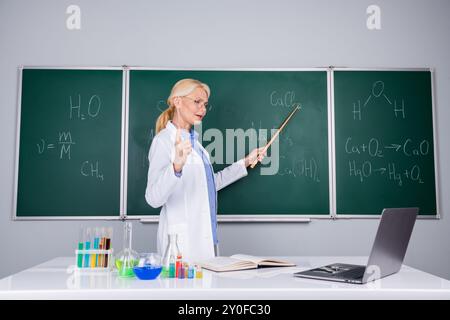 Foto einer selbstbewussten, intelligenten Frau Lehrerin tragen weißen Mantel Distanz Ausbildung isoliert auf grünem Bretthintergrund Stockfoto