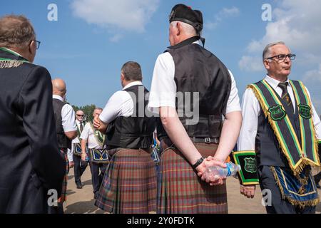 Die Mitglieder der Stranocum Royal Black Preceptory gehen an Männern vorbei, die in Kilts und Hochlandkleidung gekleidet sind und in Ballee ankommen. Ballymena, Großbritannien - 31. August 2024. Stockfoto