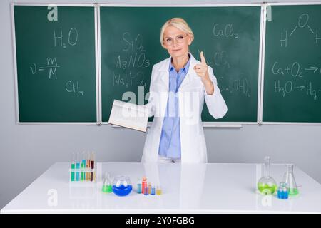 Foto einer seriösen intelligenten Seniorin tragen weißen Mantel erklären chemisches Experiment isoliert auf grünem Bretthintergrund Stockfoto