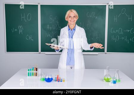 Foto der intelligenten Seniorin tragen weißen Mantel College-Vortrag erklären chemisches Experiment isoliert auf grünem Bretthintergrund Stockfoto