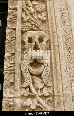 Schädel- und Kreuzknochenschnitzereien in Stein; barocke Kathedrale Monopoli italien mit Skeletten von Kardinälen, die Holztür, geschnitzte Steinschädel und das Innere Stockfoto