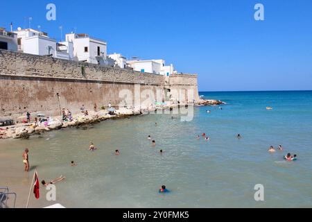 Schwimmer im Meer neben der Meeresmauer; Monopoli puglia italien - Adriaküste mit Schwimmen, Booten, Paddelbrettern, den Schutzwänden der Meeresmauer, dem Eingang aus bogenförmigem Stein, dem Meer, den Küstenfelsen, Touristen, Sportbooten, Sehenswürdigkeiten und Sonnenanbeter Stockfoto