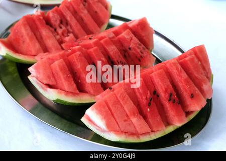 Nahaufnahme frischer Wassermelonenscheiben, ordentlich auf einer Edelstahlplatte angeordnet. Die leuchtend roten Früchte stehen im Kontrast zur glänzenden silbernen Oberfläche cr Stockfoto